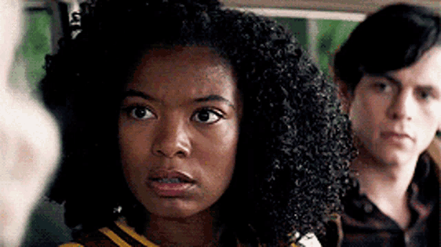 a woman with curly hair is looking at the camera while a man looks on .
