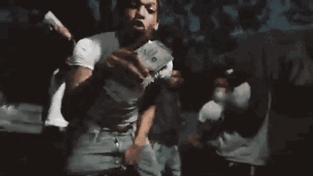 a man in a white shirt is standing in front of a group of people holding a gun .