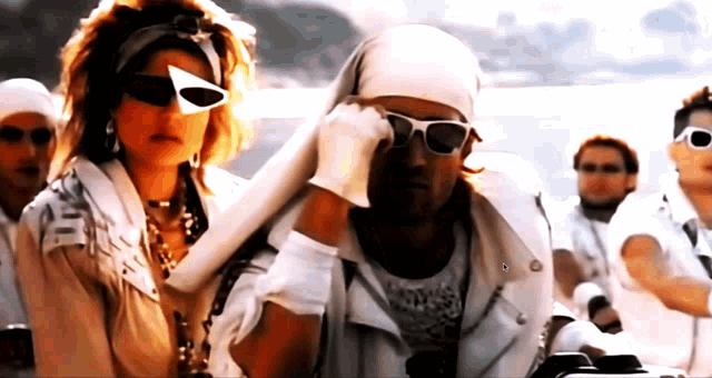 a man wearing sunglasses and a bandana stands next to a woman