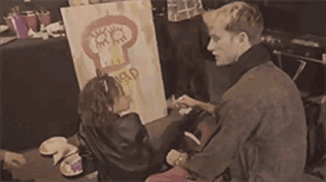 a man and a woman are sitting in front of a painting that says " mad " on it