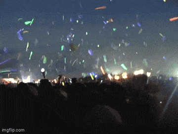 a crowd of people watching a concert with confetti falling from the sky