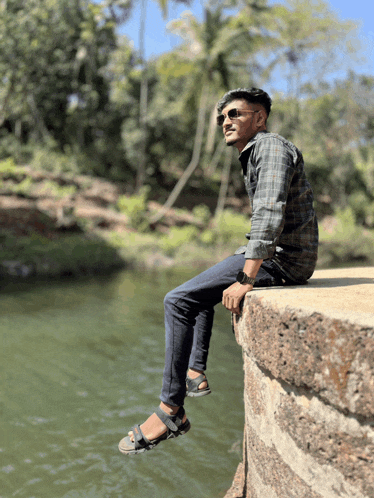 a young man sits on a ledge overlooking a river