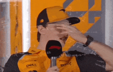 a man is covering his face with his hand while holding a microphone in front of a wall with math equations on it .