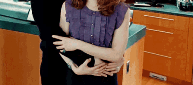 a woman in a purple top is hugging a man in a black shirt in a kitchen