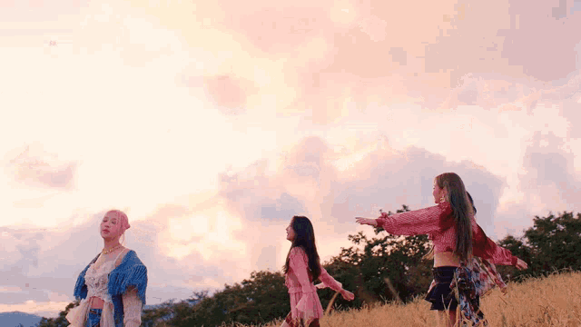 three women are standing in a field with their arms outstretched in front of a cloudy sky