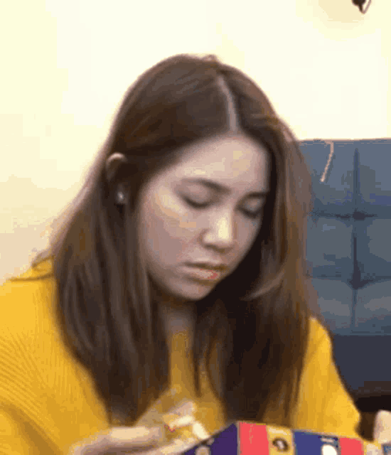 a woman in a yellow sweater is eating a candy bar