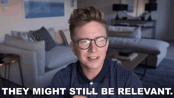 a man wearing glasses is sitting in a living room with the words `` they might still be relevant '' written on the screen .