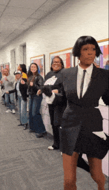 a group of people are standing in a hallway and one of them is dressed in a suit and tie