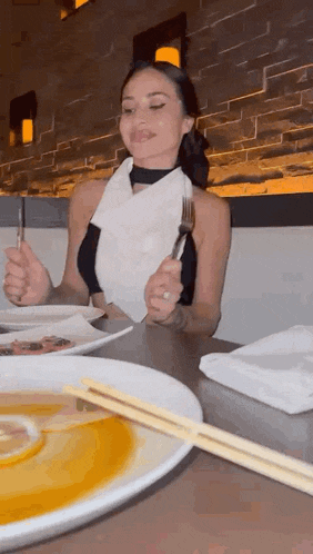 a woman is sitting at a table eating a meal with chopsticks and a fork .
