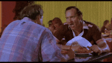 two men are sitting at a table in a restaurant and one of them is wearing a shirt that says budweiser on it