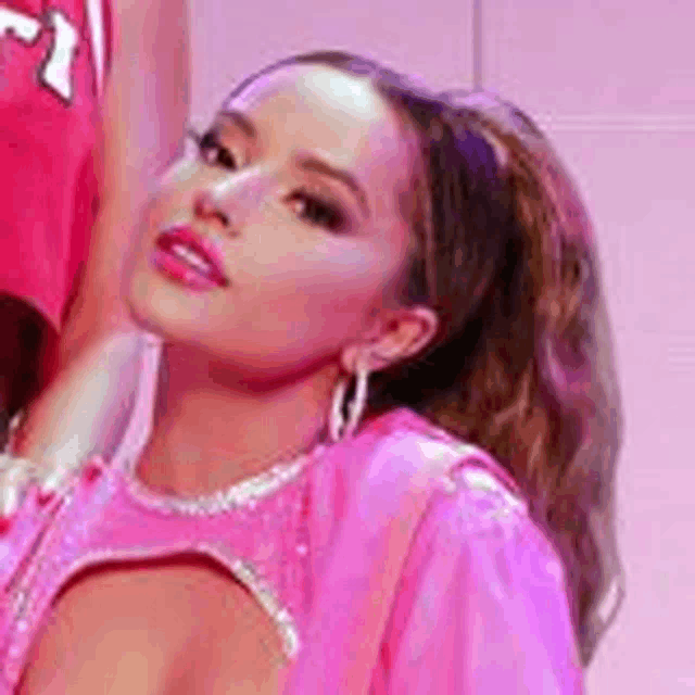 a woman in a pink dress and hoop earrings is standing in front of a pink wall .