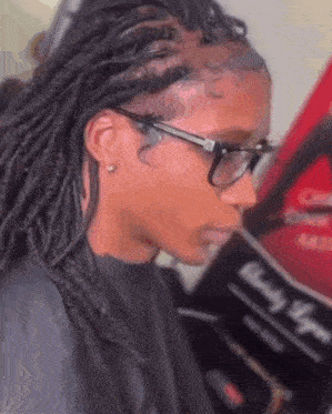 a woman wearing glasses and dreadlocks is getting her hair done at a salon .