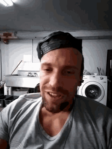 a man wearing a baseball cap is smiling in front of a washer and dryer
