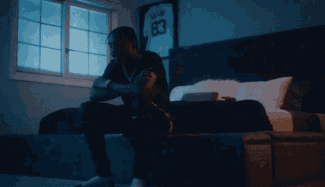 a man sits on a bed in front of a window with a jersey on the wall that says 83