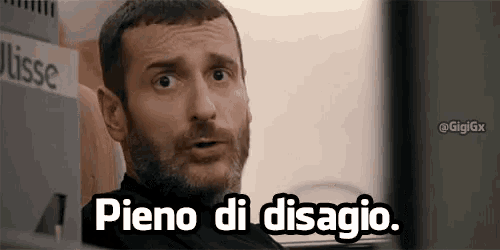 a man with a beard is sitting in front of a computer screen with the words pieno di disagio written on it .