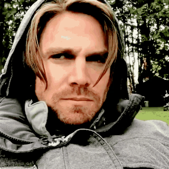 a man with long hair and a beard wearing a grey jacket with a hood