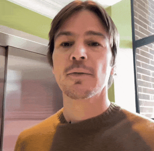 a man with a beard wearing a yellow sweater looks at the camera