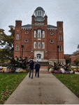 two men walking down a sidewalk in front of a large brick building