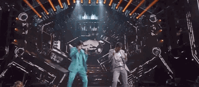 two men in suits are dancing on a stage with a lot of lights .
