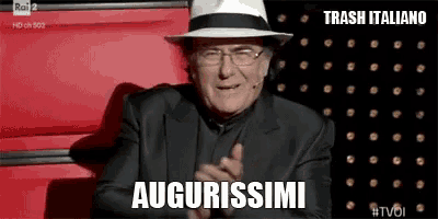 a man wearing a hat and glasses is sitting in a chair and clapping his hands .