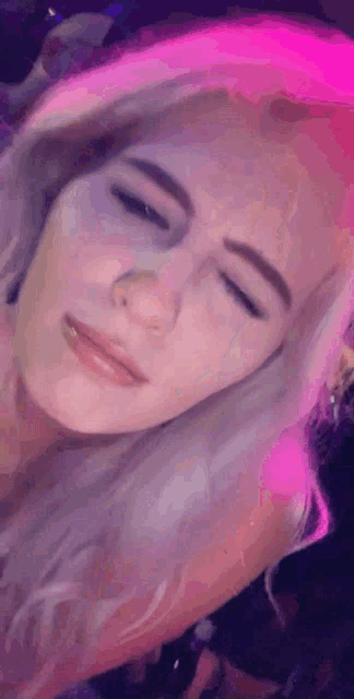 a close up of a woman 's face with her eyes closed and pink lights behind her .