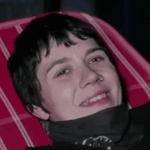 a young man with a bandana around his neck is smiling while laying in a chair .