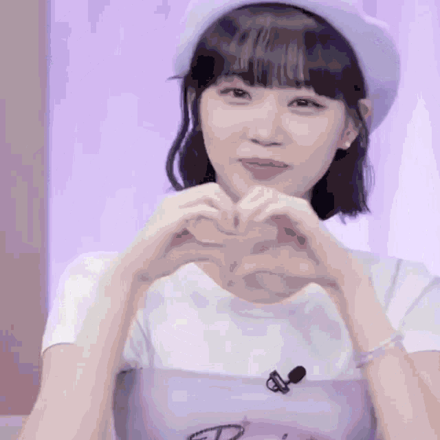 a girl in a purple hat is making a heart with her hands .