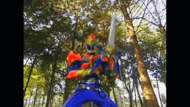 a man in a blue and orange costume is holding a sword in the woods .