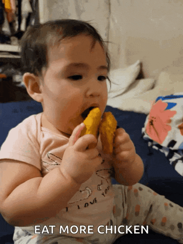 a baby in a pink shirt that says i love you is eating a piece of chicken