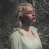 a woman in a white dress is standing in the woods .