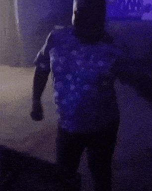 a man in a blue shirt is dancing in a dark room with purple lights