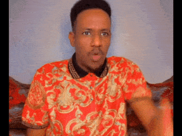 a man wearing a red and gold shirt is sitting on a couch making a funny face .