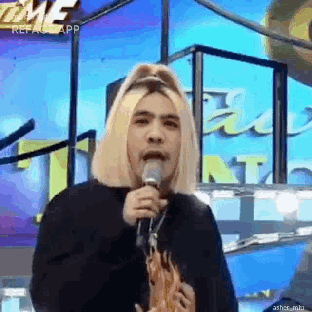 a man with blonde hair is singing into a microphone while wearing sunglasses .