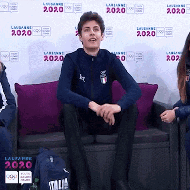 a man sits on a couch in front of a wall that says 2020