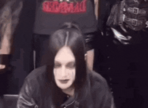 a woman with long black hair is wearing a black jacket and making a funny face in front of a group of people .