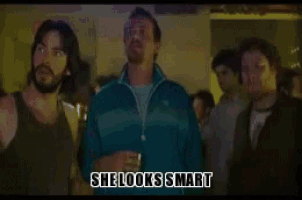a group of men are standing in a dark room and one of them is saying she looks smart