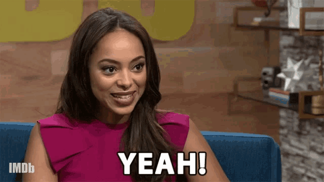 a woman in a pink top is sitting on a couch and saying yeah