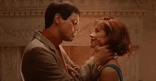 a man is holding a woman 's neck while they kiss .