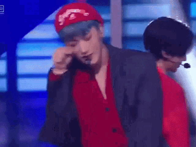 a man wearing a red hat and a red jacket is crying on stage .