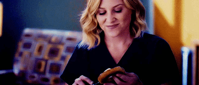 a woman is eating a hamburger in a living room .