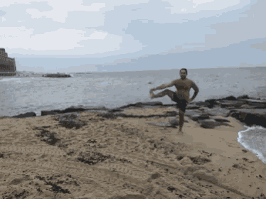 a man is standing on one leg on a beach near the ocean