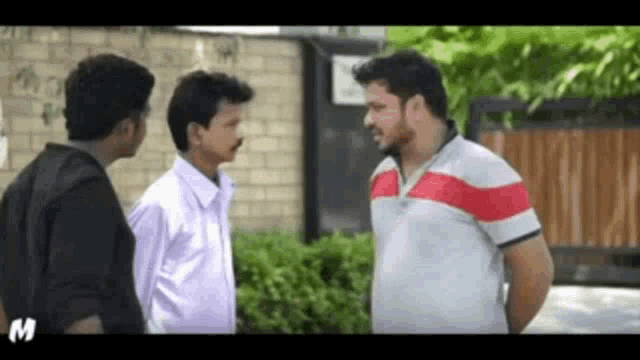 three men are standing next to each other in front of a brick wall and talking to each other .
