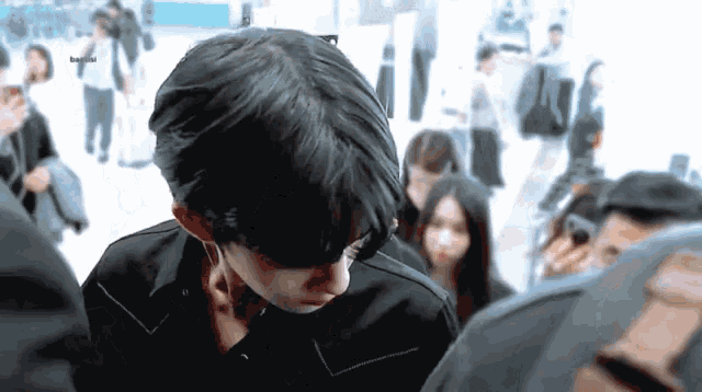 a man in a black jacket is standing in a crowd of people and looking down