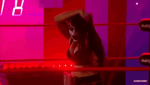 a woman is standing in a wrestling ring in a dark room with red lights .
