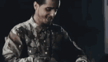 a man in a camouflage shirt is sitting in front of a computer screen .