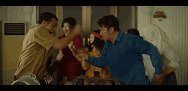 a group of people are standing around a table with a man in a blue shirt