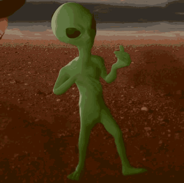 a green alien is giving a thumbs up in the dirt