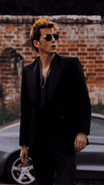 a man in a black suit and sunglasses stands in front of a car