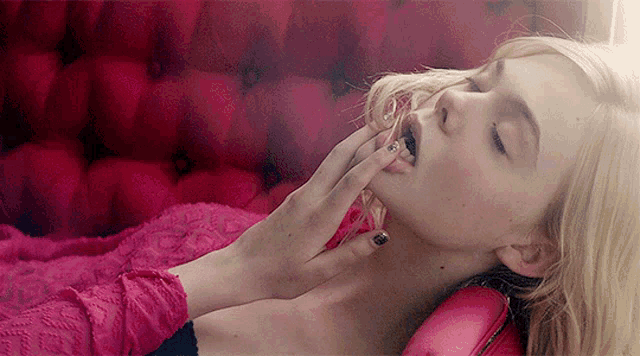 a woman is laying on a pink couch with her hand on her face