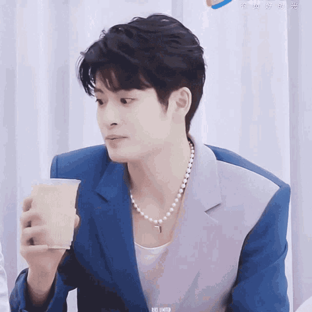 a young man wearing a pearl necklace is holding a cup of coffee .